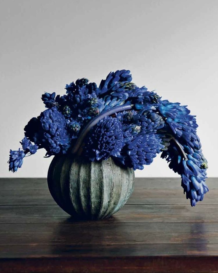 Blue flowers in a textured green vase on a wooden surface with a neutral background