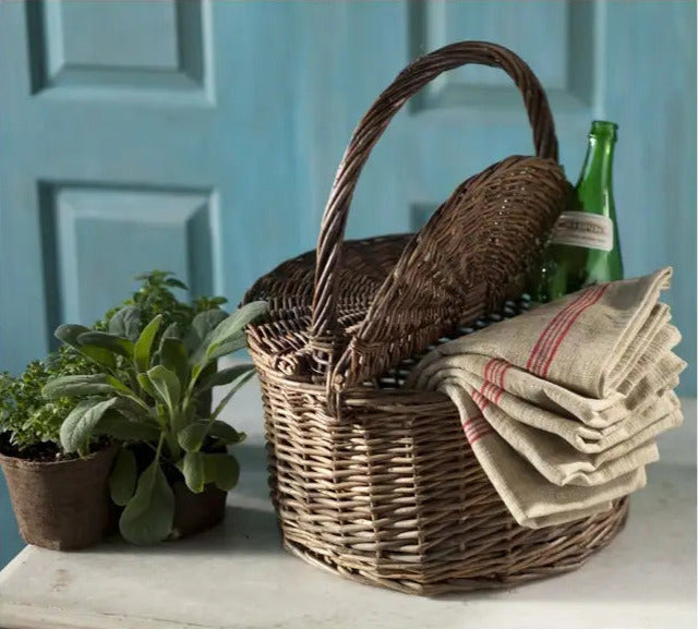 Wicker picnic basket with a bottle, napkins, and plants on a table against a blue wall.