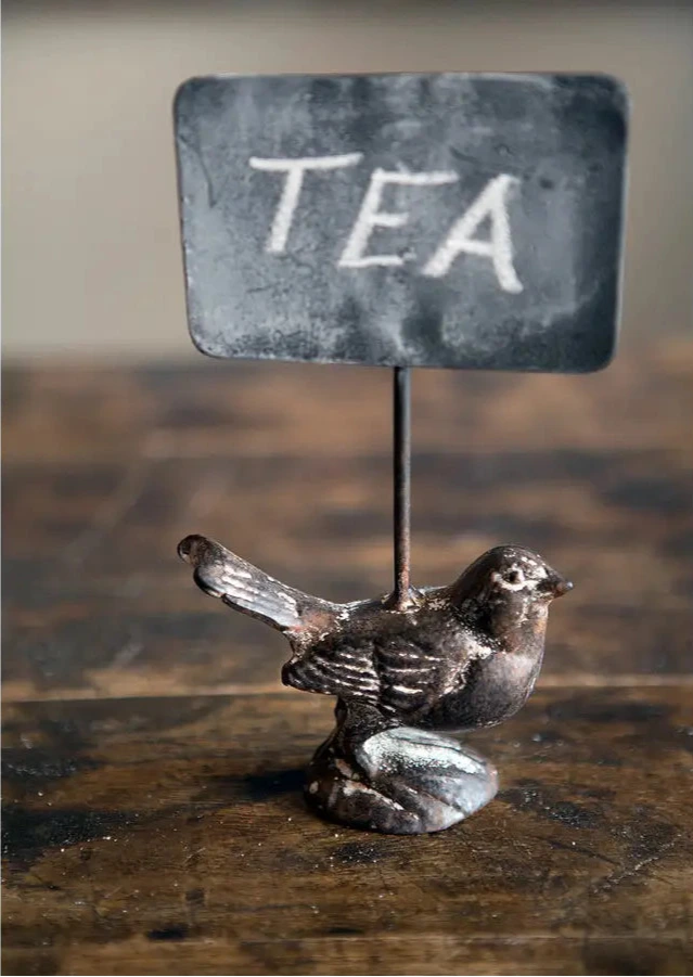 Metallic bird figurine with a 'TEA' sign on a wooden surface